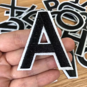 May include: Black felt letter A with white outline. The letter is iron-on and can be used to personalize clothing, bags, and other items.