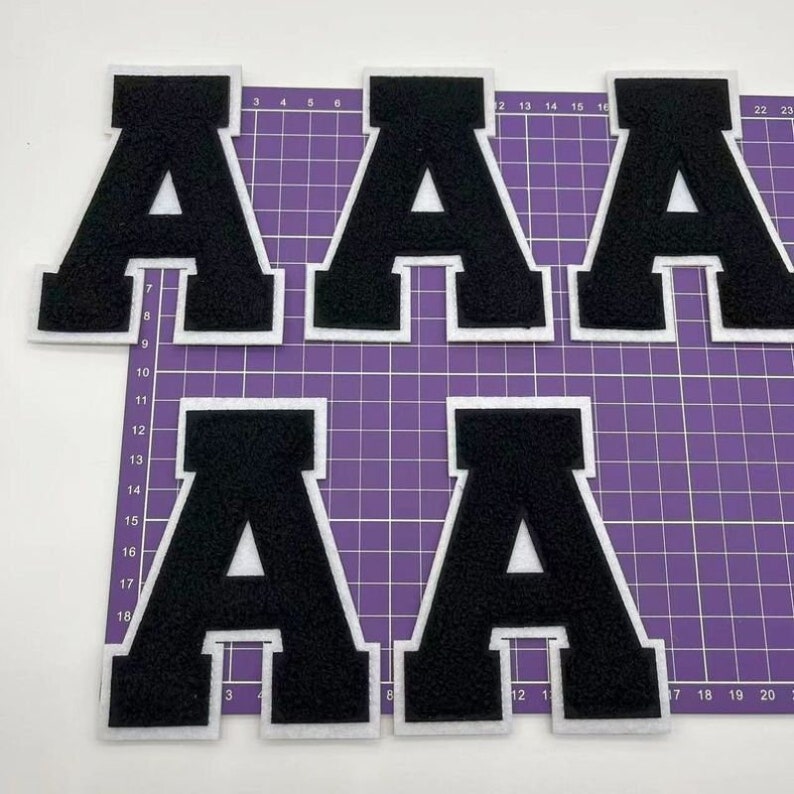 K&ouml;nnte beinhalten: Vier schwarze Filzbuchstaben-Patches in Form des Buchstabens A. Die Patches sind wei&szlig; umrandet und haben einen wei&szlig;en Hintergrund.