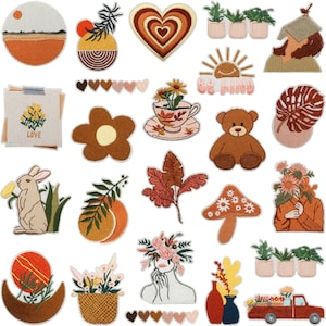 May include: A collection of embroidered patches in warm earth tones. Designs include a heart, flowers, a rabbit, a mushroom, a teddy bear, and a red truck. Some patches feature the words "LOVE" and "BE KIND".