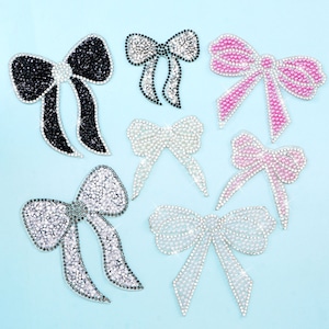 May include: A set of six rhinestone bow appliques in various colours, including black, white, and pink. The bows are made of small, sparkling rhinestones and are perfect for adding a touch of sparkle to any project.