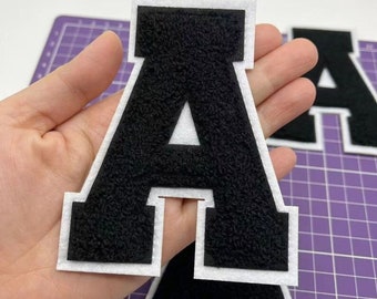 May include: Black felt letter A with white outline. The letter is thick and has a fuzzy texture.
