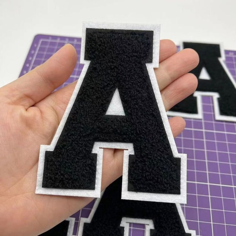 K&ouml;nnte beinhalten: Schwarzer Filzbuchstabe A mit wei&szlig;em Umriss. Der Buchstabe ist dick und hat eine flauschige Textur.