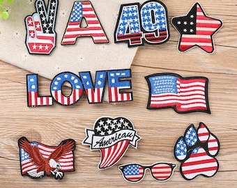 Può includere: Un set di dieci toppe da stirare con disegni di bandiere americane. Le toppe includono un segno di pace, la lettera A, il numero 49, una stella, la parola LOVE, una bandiera, un cuore con la parola "American" su di esso, un'impronta di zampa e un paio di occhiali.