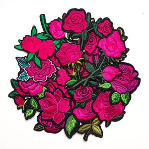 Op de afbeelding: Een verzameling geborduurde rozenpatches met levendige felroze en magentakleurige bloemblaadjes en heldergroene bladeren en stengels. Elke individuele rozenpatch is omlijnd met zwart garen, wat zorgt voor een dicht cluster van bloemmotieven.