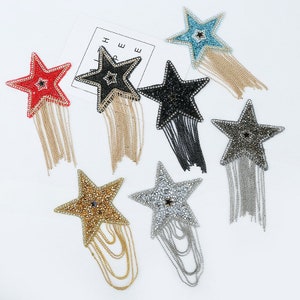 May include: Seven star-shaped iron-on patches with dangling chains. The stars are embellished with rhinestones in various colors, including red, black, gold, silver, and blue.