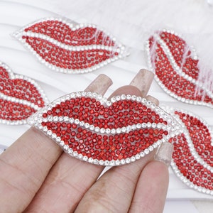 May include: Red rhinestone lips with a clear plastic backing. The lips are a popular embellishment for clothing, bags, and other accessories.