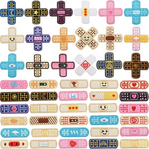 May include: A collection of decorative adhesive bandages and cross-shaped patches in various colors and designs. The patches feature patterns like stars, moons, hearts, and smiley faces. The bandages also have different patterns and text.