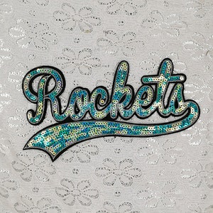 Op de afbeelding: Een strijkbare patch met het woord "Rockets" in een cursief schrift, gemaakt van blauwe en groene pailletten.