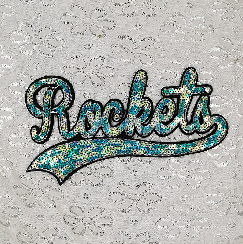 Op de afbeelding: Een strijkbare patch met het woord "Rockets" in een cursief schrift, gemaakt van blauwe en groene pailletten.