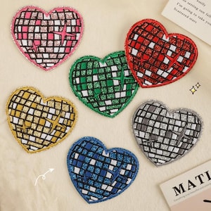 Pode incluir: Seis patches termocolantes em forma de coração com um design de bola de discoteca. Os patches são de várias cores, incluindo rosa, vermelho, verde, dourado, prateado e azul.