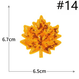 Pu&ograve; includere: Una toppa a forma di foglia d'acero etichettata #14, ricoperta di paillettes arancioni scintillanti con un bordo ricamato giallo. La toppa misura 6,7 cm in altezza e 6,5 cm in larghezza, come indicato dalle linee di misura e dal testo.