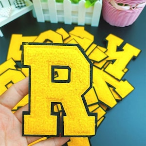 May include: A close-up of a yellow felt letter R with a black outline. The letter is part of a set of letters, all of which are yellow with black outlines.