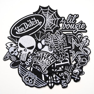 Peut inclure: Un assortiment d'écussons brodés noirs et blancs. Les motifs comprennent une tête de mort, une toile d'araignée, un scorpion, une étoile et des textes tels que "Von Dutch", "We're all mad here" et "Route 66".