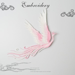 May include: Pink and white embroidered phoenix applique patch. The phoenix is flying with its wings spread and its tail feathers trailing behind it.