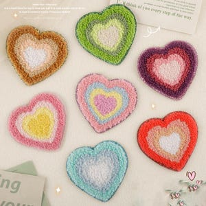 Peut inclure: Six patchs en feutre en forme de cœur de différentes couleurs avec un plus petit cœur au centre. Les cœurs sont superposés dans des tons de rose, jaune, vert, bleu, orange et violet.