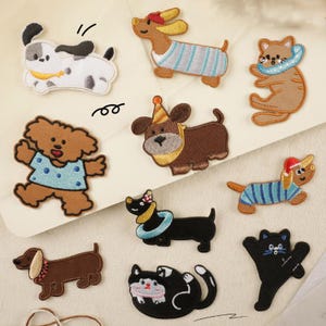 May include: A set of 10 embroidered iron-on patches featuring various cartoon dogs and cats. The patches are colourful and feature different designs, including a dog wearing a party hat, a cat wearing a life preserver, and a dog wearing a striped shirt.