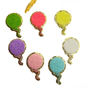 May include: Seven colorful felt balloon patches with gold glitter trim and gold string accents. The balloons are green, pink, yellow, white, light pink, light blue, and purple.