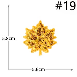 Pu&ograve; includere: Una toppa a forma di foglia d'acero con paillettes dorate etichettata #19. La toppa presenta una disposizione densa di piccole paillettes dorate riflettenti su una base in tessuto. Le linee di misura indicano 5,8 cm di altezza e 5,6 cm di larghezza.