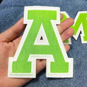 May include: A bright green felt letter A with white outlining. The letter is a large, thick, felt patch.