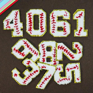 Op de afbeelding: Witte baseball-thema nummerpatches met rode stiksels en gouden rand. De nummers zijn 4, 0, 6, 1, 9, 8, 7 en 5. Deze patches zijn waarschijnlijk voor sportshirts of knutselwerk.