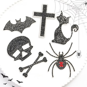 May include: A collection of black rhinestone Halloween-themed embellishments. Includes a bat, cross, cat, skull, crossbones, and spider with a red accent. Perfect for crafting or adding spooky flair to projects.