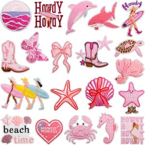 Peut inclure: Une collection d'écussons brodés roses sur les thèmes de la plage et du littoral. Les motifs comprennent un dauphin, un requin, une étoile de mer, un coquillage, un hippocampe, des bottes de cow-boy, un papillon et du texte qui dit "Howdy" et "Beach Time".