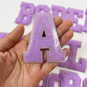 Peut inclure: Lettres en feutre violet en forme de lettres "B", "O", "D", "E", "A", "L", et "Y".