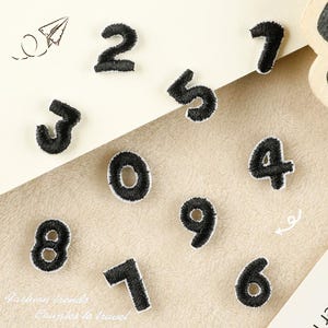 Pode incluir: Dez patches termocolantes pretos com os números de 0 a 9. Os patches estão sobre uma superfície branca.