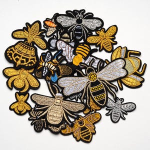 May include: A selection of embroidered bee patches in various sizes and colours. The patches feature detailed designs with gold, silver, black, and yellow threads. These patches are ideal for adding decorative accents to clothing or accessories.