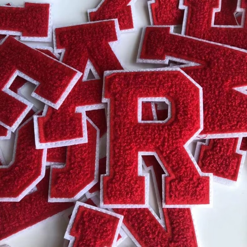 Op de afbeelding: Een stapel rode vilt letter patches met witte randen. De letters zijn allemaal in hoofdletters en omvatten de letters S, R en A.