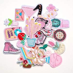 May include: A collection of embroidered patches in various shapes and colors. Designs include a pink cocktail, cactus, strawberry, high-top sneaker, and patches with the words "LOVE" and "HAPPY DAYS". The patches have white borders.