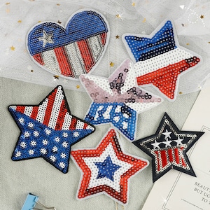 May include: Six iron-on patches featuring stars and hearts in red, white, and blue with a sequined design. The patches are perfect for adding a patriotic touch to clothing, bags, or other accessories.