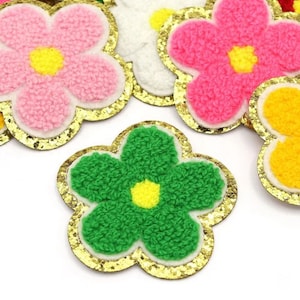 May include: Assortment of colorful felt flower patches with gold glitter trim. The flowers are pink, green, white, and yellow.