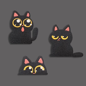 May include: Three black cat patches with embroidered details. One cat has wide eyes and an open mouth, another has a grumpy expression, and the third is peeking out. Each cat has yellow eyes and pink inner ears.