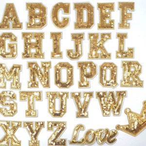 Peut inclure: Ensemble de lettres de l'alphabet dorées à paillettes, une couronne et le mot "Love" sur fond blanc. Les lettres sont dans un style bloc audacieux, chacune découpée individuellement. La couronne et le mot "Love" sont également dorés à paillettes.