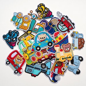 May include: A selection of colourful embroidered patches depicting different vehicles such as cars, trains, scooters, and aeroplanes. Each patch has a cartoon design with vibrant colours and detailed stitching. Some patches feature cute bear characters.