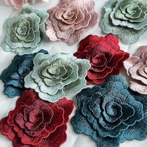 May include: Assortment of embroidered fabric flower appliques in various colors, including teal, green, burgundy, and pink. The flowers are layered and have a 3D effect.