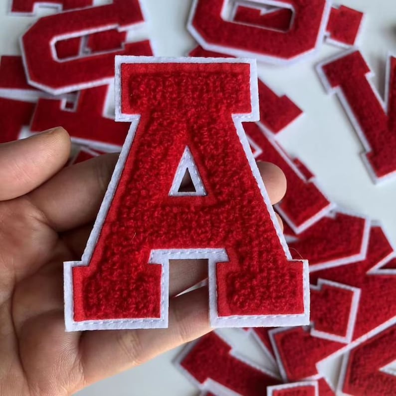 Op de afbeelding: Rode viltletter A met een witte omtrek. De letter is groot, vetgedrukt en in hoofdletters. De letter is een patch of strijklabel.
