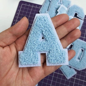May include: Light blue felt letter A with a white backing. The letter is fuzzy and has a raised design.