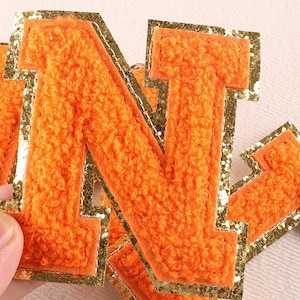 May include: Orange felt letter N with gold glitter trim. The letter is thick and has a fuzzy texture.