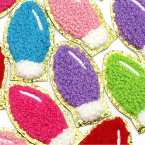 Peut inclure: Assortiment de patchs en forme d'ampoule de lumière moelleux et colorés avec une bordure dorée scintillante. Les patchs sont roses, bleus, violets, verts et rouges.