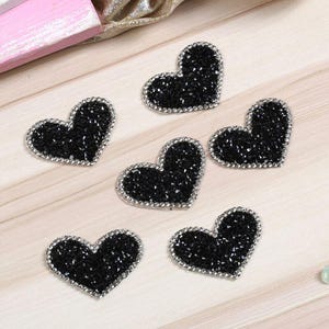 May include: Six black heart-shaped iron-on patches with silver glitter embellishments.