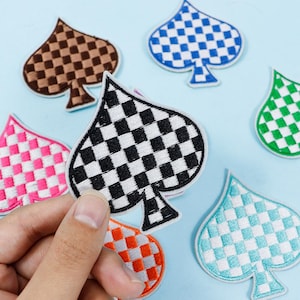 May include: A selection of embroidered spade-shaped patches in various colours and checkered patterns. The patches include black and white, brown, blue, green, pink, orange, and turquoise designs. These patches are likely intended for decorative use on clothing or accessories.