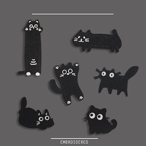 May include: A collection of black embroidered cat patches in various poses. Each patch features white details for the eyes, whiskers, and paws. The word "EMBROIDERED" is printed in white at the bottom of the image.