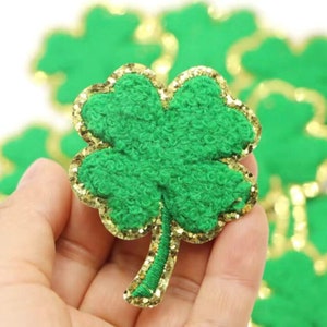 Può includere: Trifoglio in feltro verde con contorno di glitter dorato. Il trifoglio è un simbolo popolare di buona fortuna e viene spesso utilizzato per le decorazioni del giorno di San Patrizio.