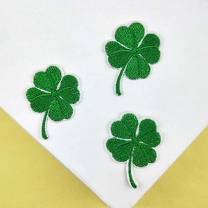 May include: Three green four-leaf clover embroidered patches on a white background.