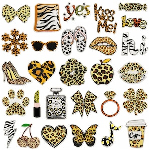 May include: A selection of iron-on patches with diverse designs. Features leopard print patterns, text, and shapes such as a bow, lips, heart, and high heels. The patches use a mix of colours, including black, white, and orange.