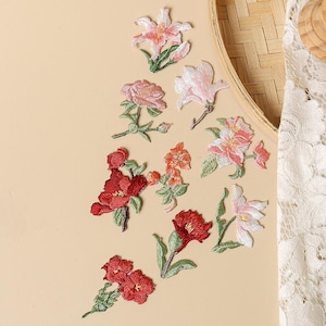May include: A collection of ten individual floral embroidered patches featuring various flower shapes and sizes. The designs include shades of red, pink, white, and orange, each with green stems and leaves, rendered in detailed thread work.