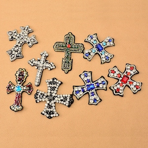 May include: Assortment of nine rhinestone cross patches in various colors, including red, blue, black, and green. The crosses are embellished with sparkling rhinestones.