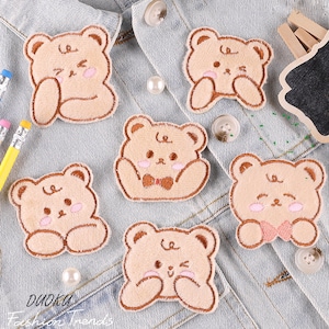 Pode incluir: Cinco patches bordados para passar a ferro com desenhos de ursos de desenho animado adoráveis com diferentes expressões. Os ursinhos são marrons com bochechas cor-de-rosa e usam uma gravata borboleta. Os patches são perfeitos para adicionar um toque de fantasia à roupa, às malas ou a outros acessórios.
